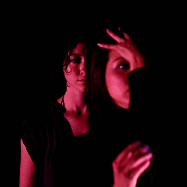 A hand presses against the forehead of a face with a figure standing behind her