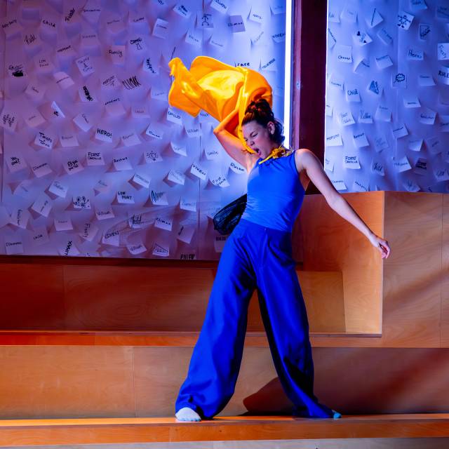 a woman dressed in blue throws back her yellow cape