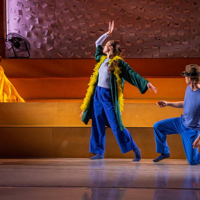 a woman dressed in blue with a yellow boa around her neck presents her hand to a guy who is on one knee
