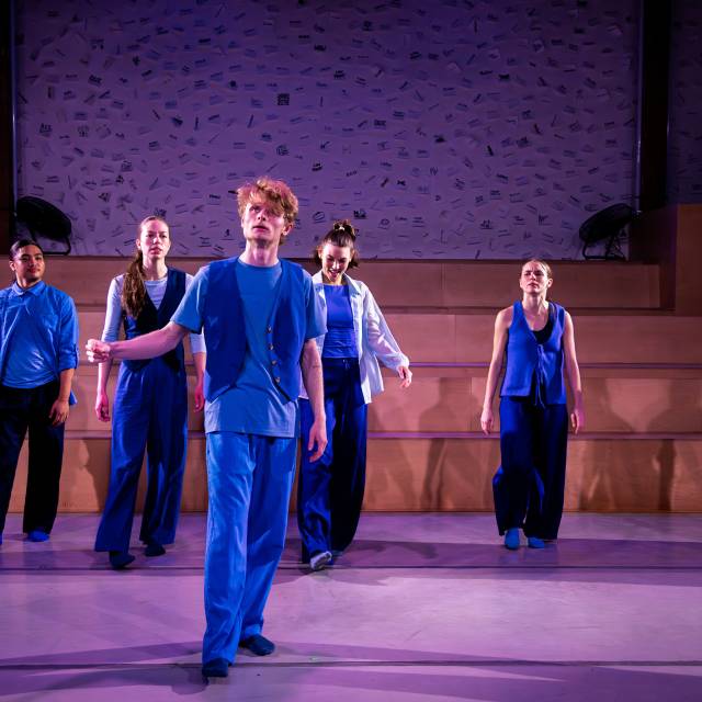 a man stands with 5 people behind him. all are dressed in blue.